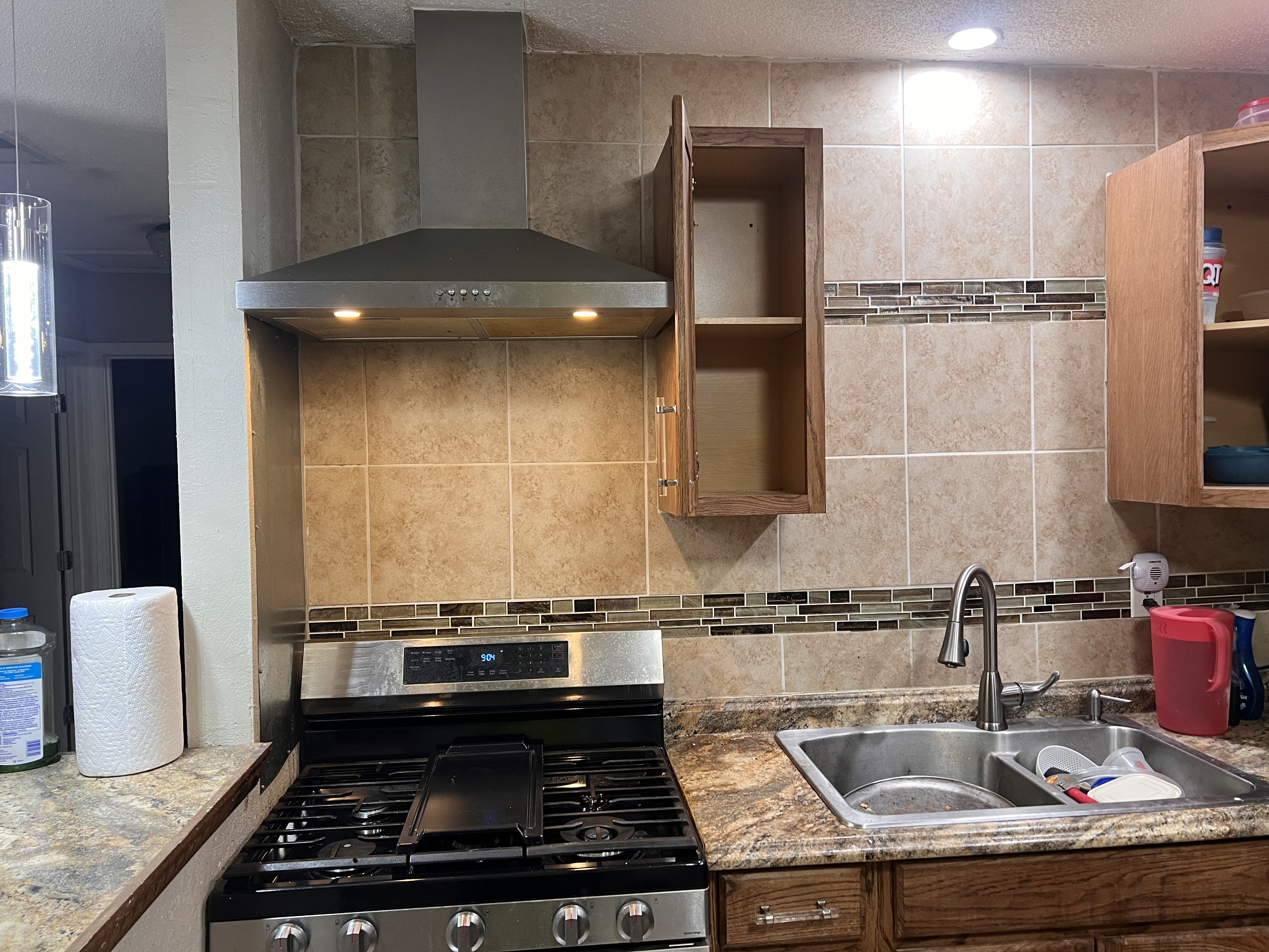 Kitchen stove and range hood beside the sink and wood cabinets